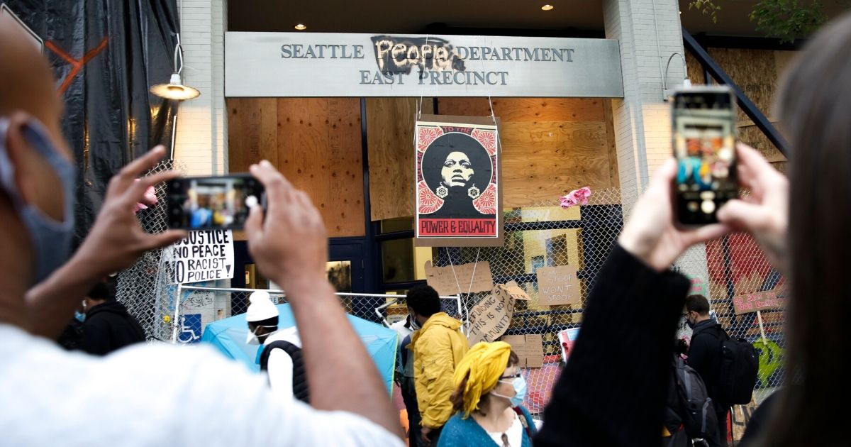 Spectators photograph an image of activist Angela Davis on display above the Seattle Police Department's now-abandoned East Precinct in the area of the city now occupied by protesters.