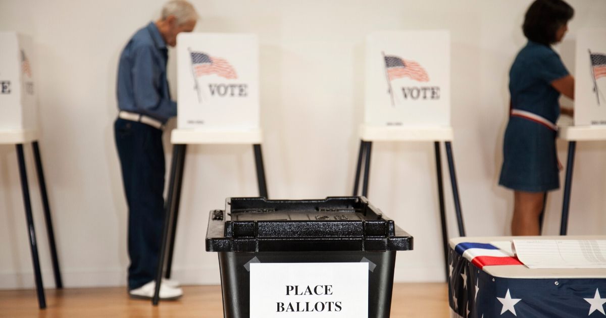 Stock image of a ballot box with voters in the background.