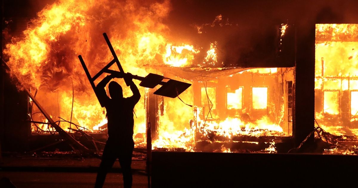 A man holds up a sign near a burning building during riots in Minneapolis on May 29, 2020.