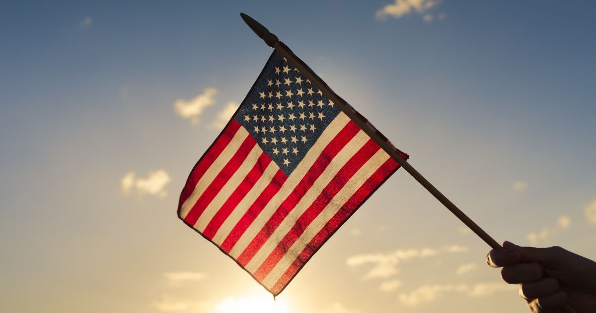 Stock image of an American flag with the sun in the background.