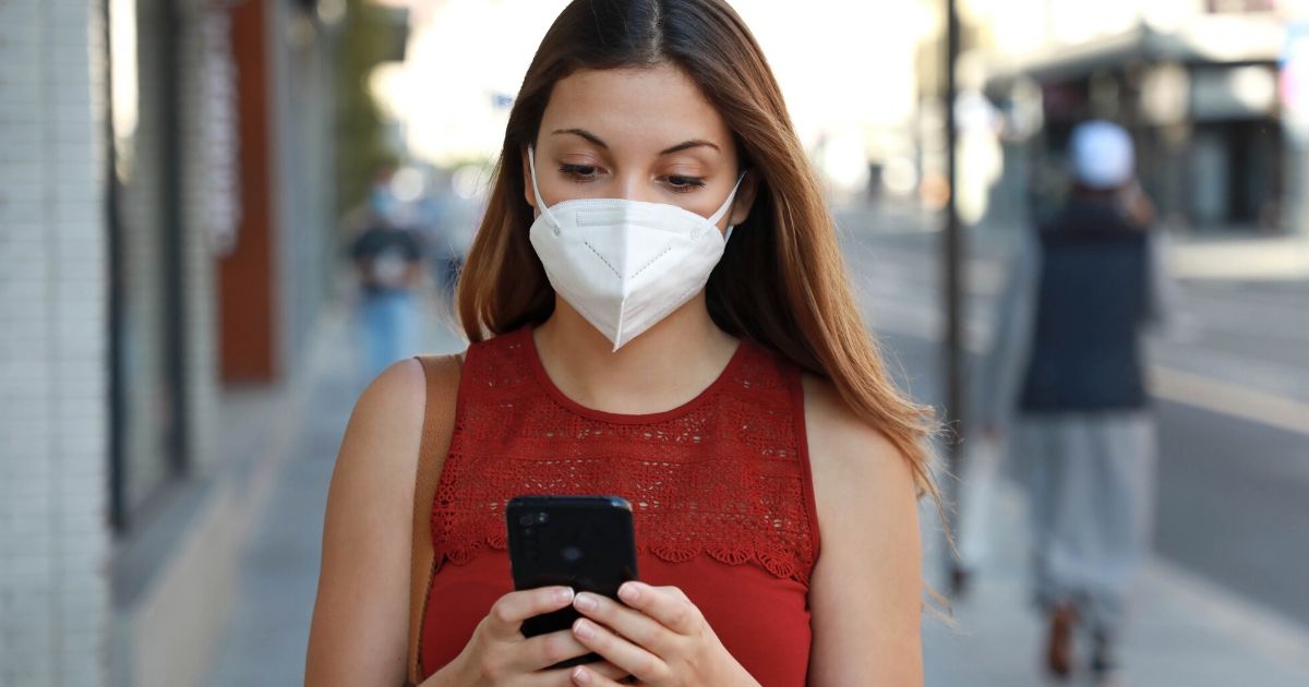 A woman wearing a protective mask looks at her phone.
