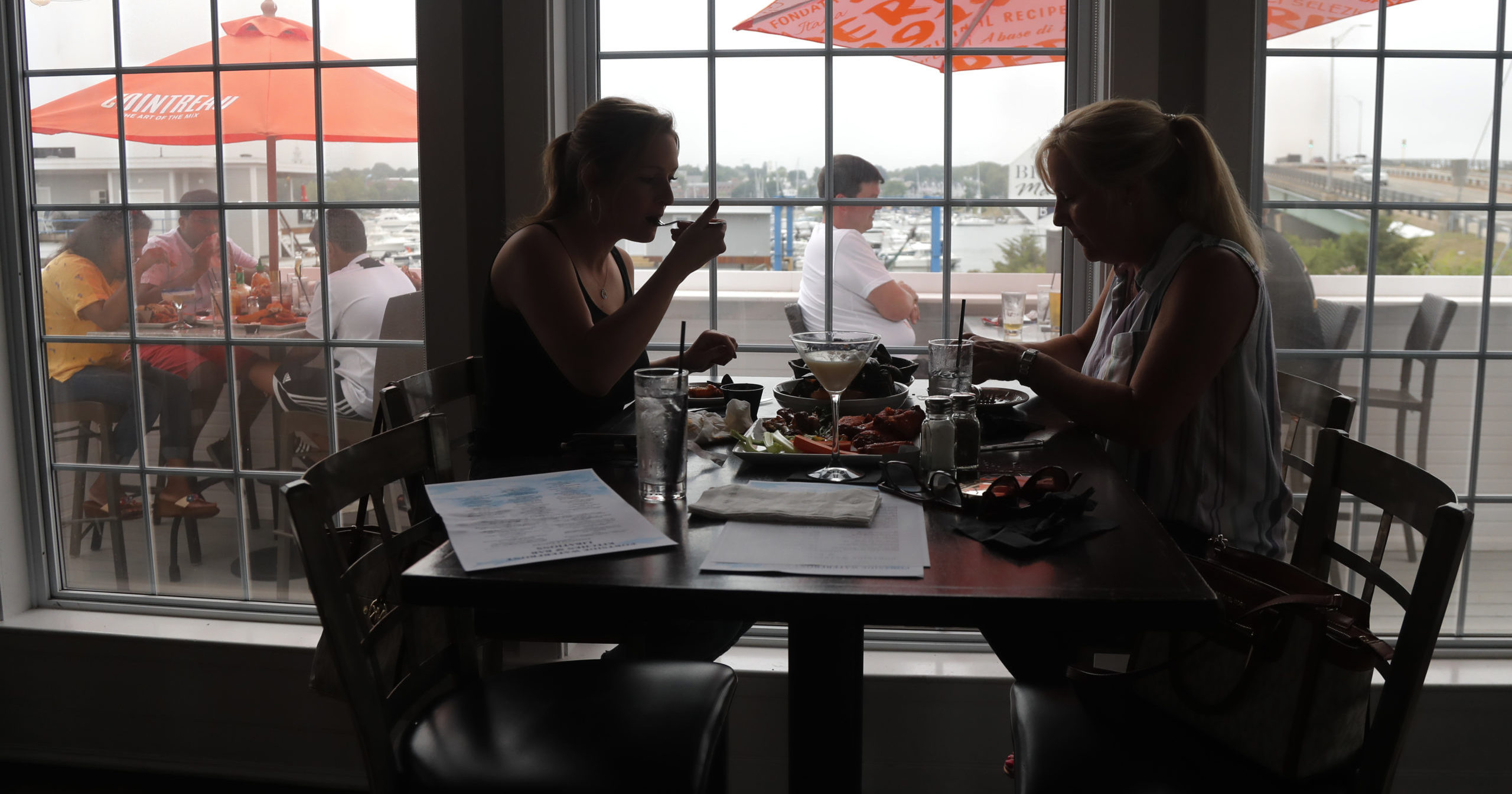 In this June 22, 2020, file photo, two women eat lunch at Portside Restaurant in Salisbury, Massachusetts, after state guidelines allowed for indoor dining. A new poll from The Associated Press-NORC Center for Public Affairs Research shows Americans becoming less concerned about infection and less supportive of restrictions.