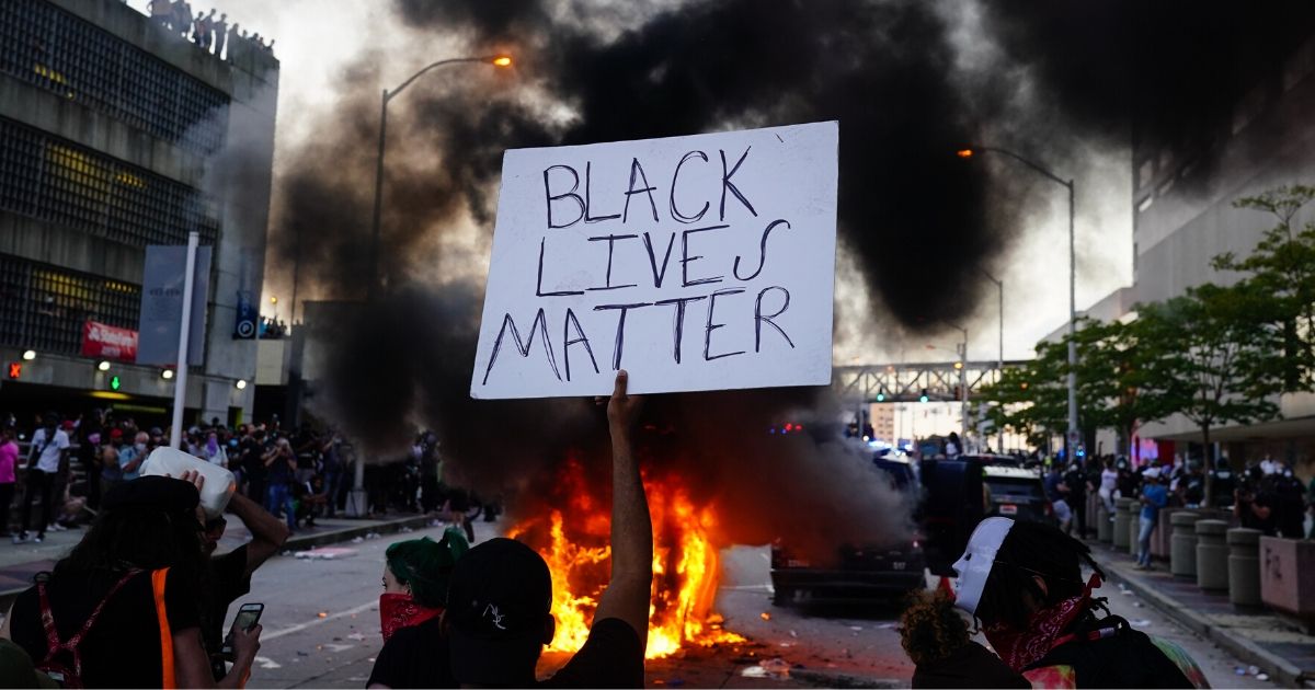 A man holds a Black Lives Matter sign as a police car burns during a protest on May 29, 2020, in Atlanta, Georgia.