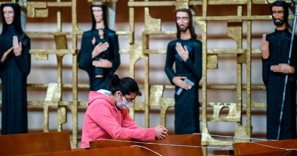 A woman wearing a face mask prays at the Sagrada Familia church on May 14, 2020, in Mexico City.