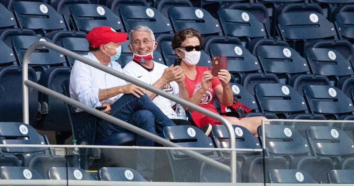 Dr. Anthony Fauci, director of the National Institute of Allergy and Infectious Diseases, center, smiles as he watches an opening day baseball game between the Washington Nationals and the New York Yankees at Nationals Park on July 23, 2020, in Washington.