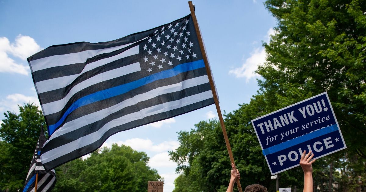 A demonstrator holds a "Thin Blue Line" flag and a sign in support of police during a protest outside the governor's mansion on June 27, 2020, in St. Paul, Minnesota.