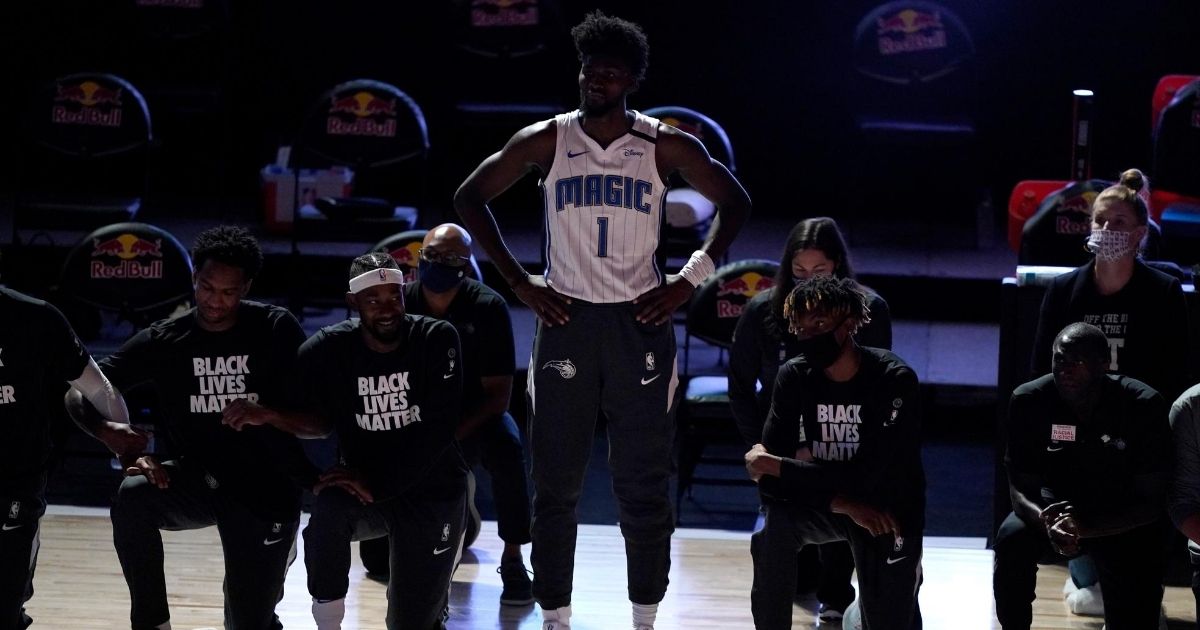 The Orlando Magic's Jonathan Isaac (1) stands as others kneel before the start of an NBA basketball game between the Brooklyn Nets and the Orlando Magic on July 31, 2020, in Lake Buena Vista, Florida.