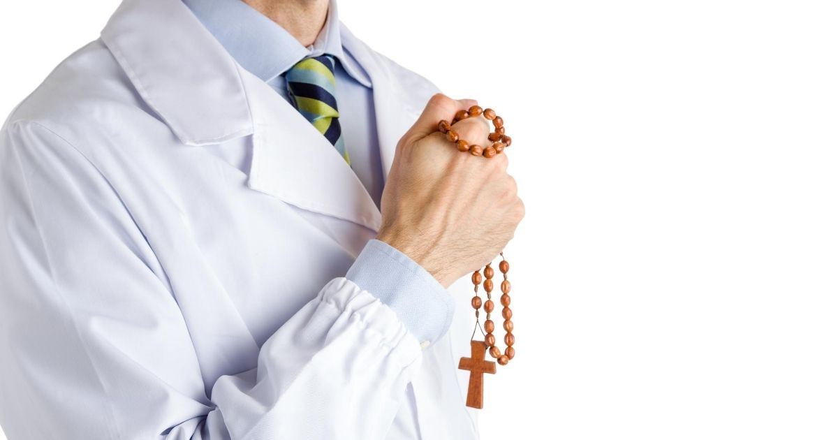 A man in a white coat holding rosary beads is seen in the stock image above.