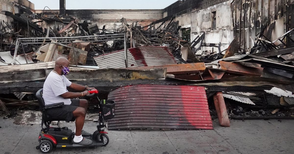 A man rides a scooter past the charred wreckage of a building in Minneapolis on June 2, 2020.