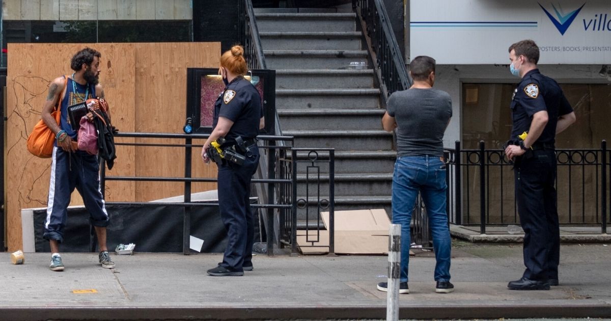NYPD officers remove a homeless person who has been "living" in front of a closed boarded up restaurant near Union Square on June 25, 2020, in New York City.