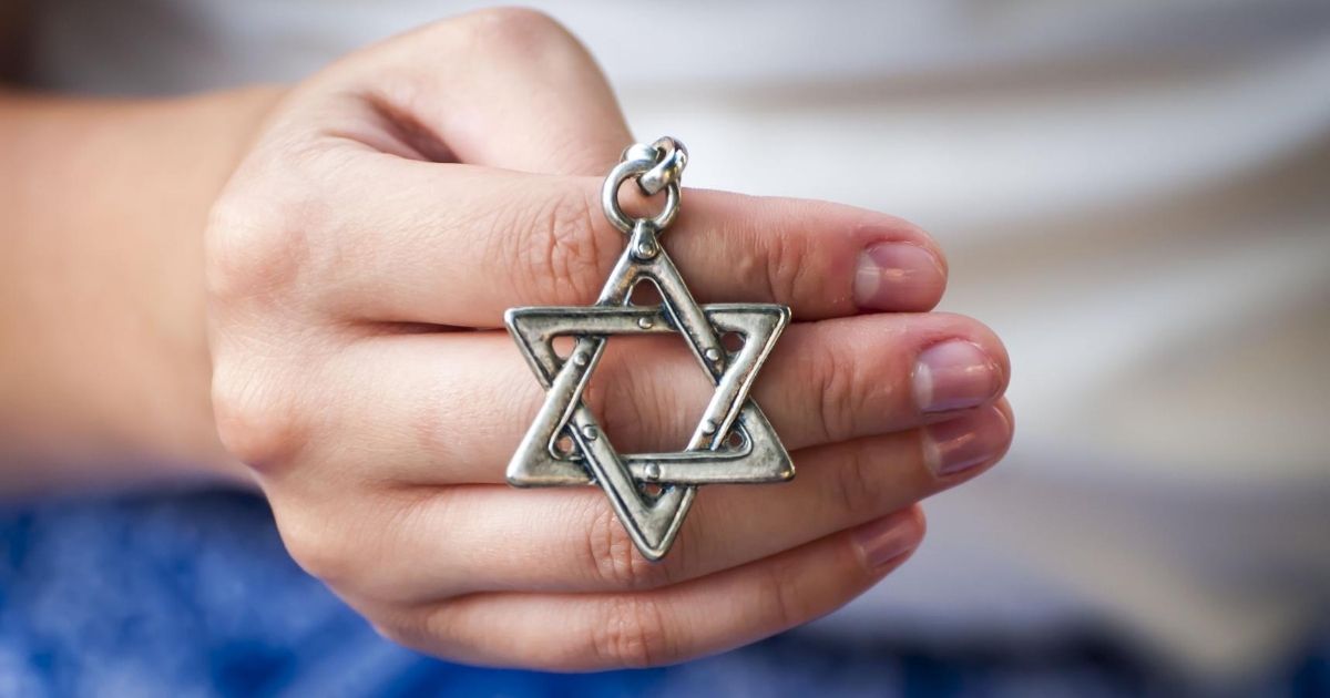 A young woman's hand holds a Star of David pendant.