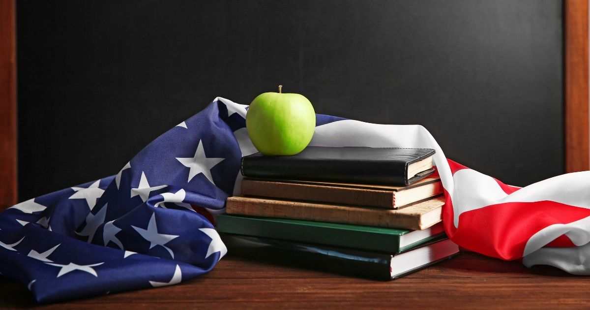 American flag with books and apple on chalk board background.