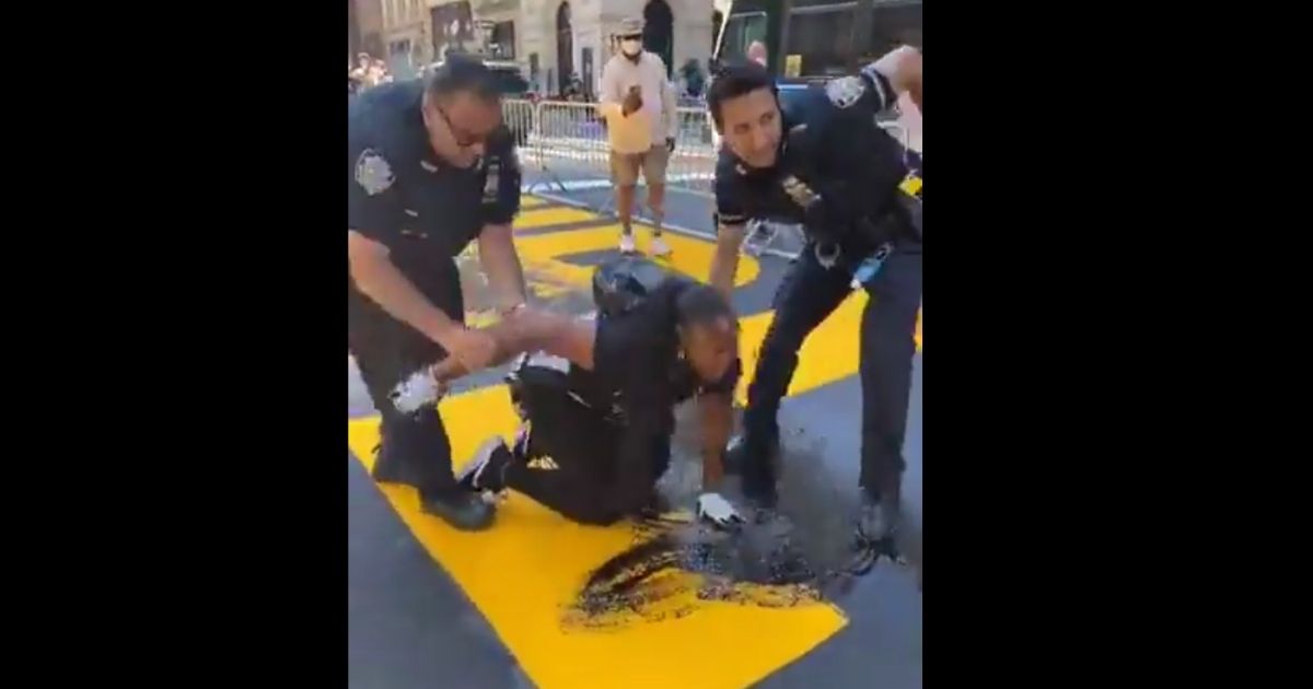 Activist Bevelyn Beatty is restrained by police after pouring paint on a Black Lives Matter street mural in New York City.