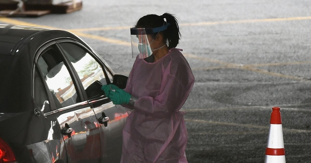 A health care worker collects a sample from a motorist in April at a Brooklyn, New York,  COVID-19 drive-thru testing site.