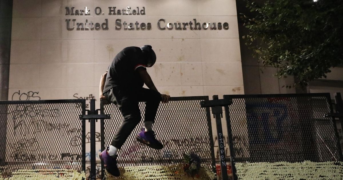 A protester climbs the fence in front of the Mark O. Hatfield federal courthouse in downtown Portland, Oregon, as the city experiences another night of unrest on July 26, 2020.