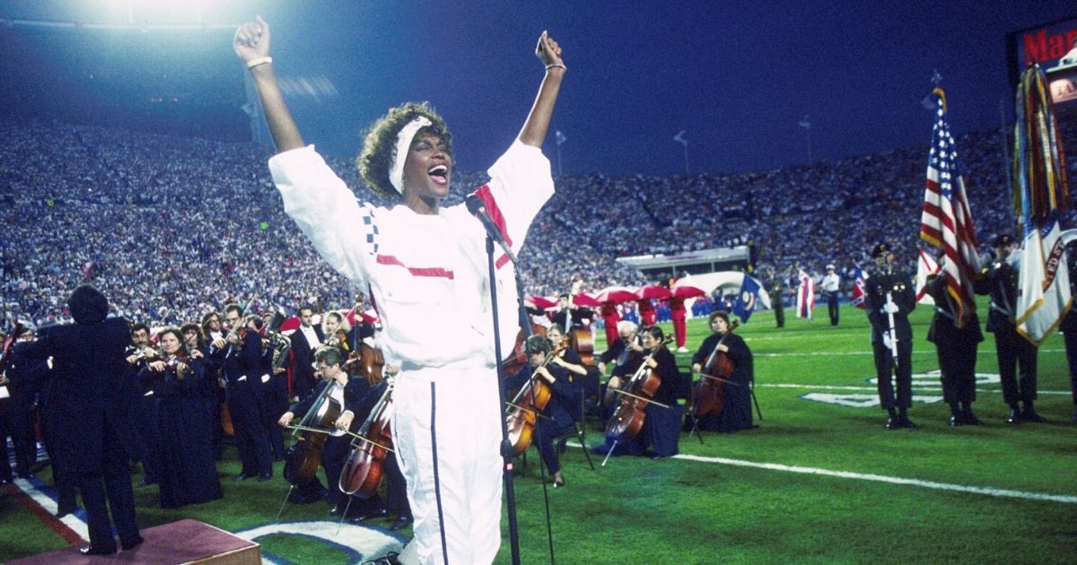 Whitney Houston sings the national anthem before Super Bowl XXV while tens of thousands of football fans wave tiny American flags in an incredible outburst of patriotism during the Persian Gulf War on Jan. 27, 1991, in Tampa, Florida.