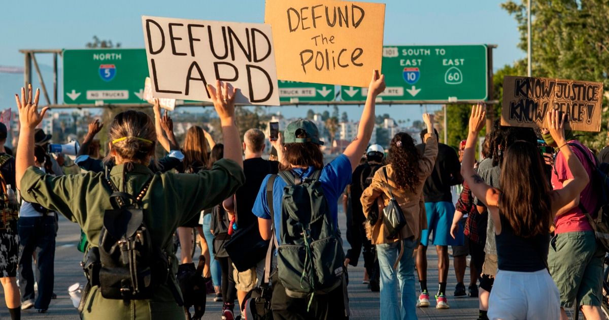 Protesters hold up signs as they block the freeway during a demonstration calling for the removal of District Attorney Jackie Lacey and to defund the police in Los Angeles on July 1, 2020.
