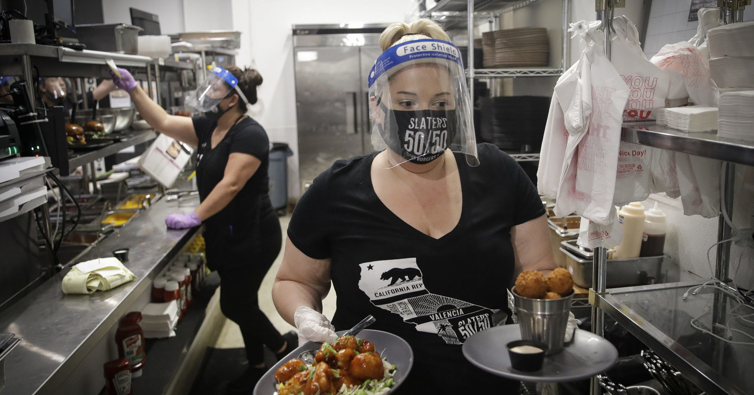 In this July 1, 2020, file photo, a waitress takes a food order from the kitchen at Slater's 50/50 in Santa Clarita, California. Gov. Gavin Newsom announced a new process on Aug. 28, 2020, for reopening California businesses that is more gradual than the state's current rules.