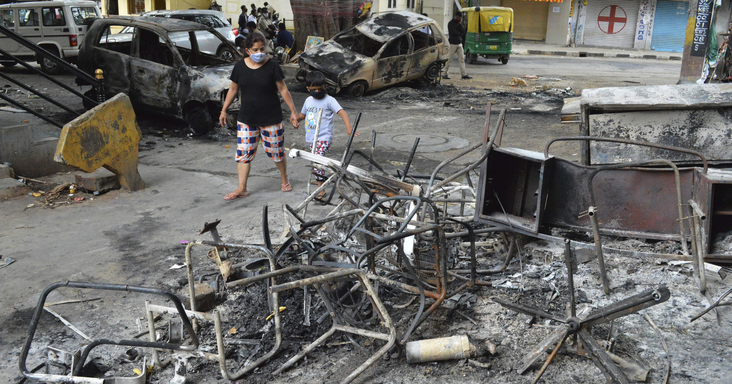 A woman and a child walks past the wreckage of vehicles and furniture burnt during violent protests in Bengaluru, India, on Aug. 12, 2020. At least three people have died in the southern Indian city also known as Bangalore after hundreds of demonstrators clashed with the police overnight against a Facebook post considered offensive to Muslims, attacking a police station and setting fire to vehicles, police said.