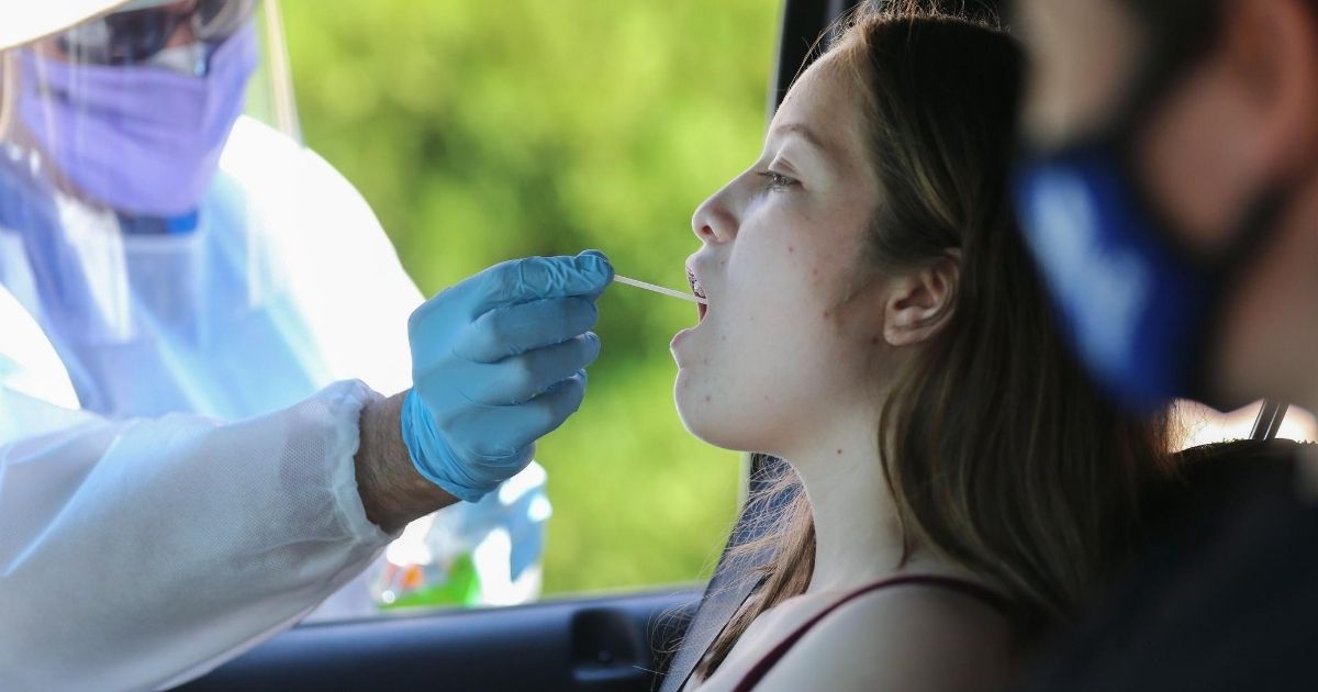A health care worker gives a girl a throat swab test at a drive-in coronavirus testing center in Los Angeles.