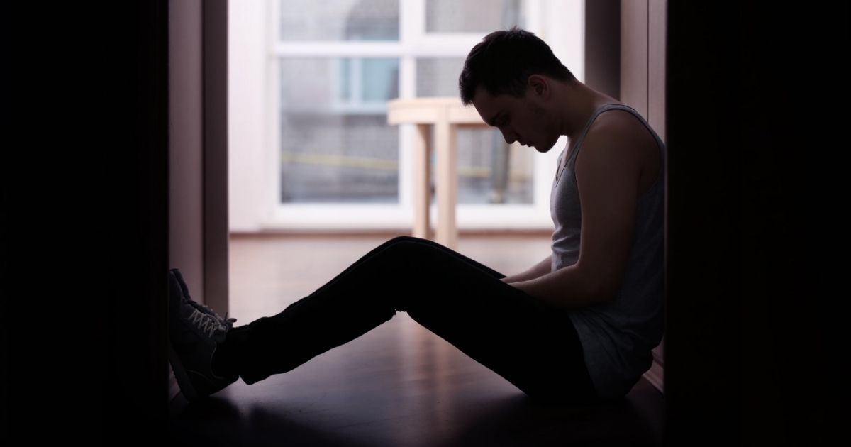 A depressed man sitting on the floor.