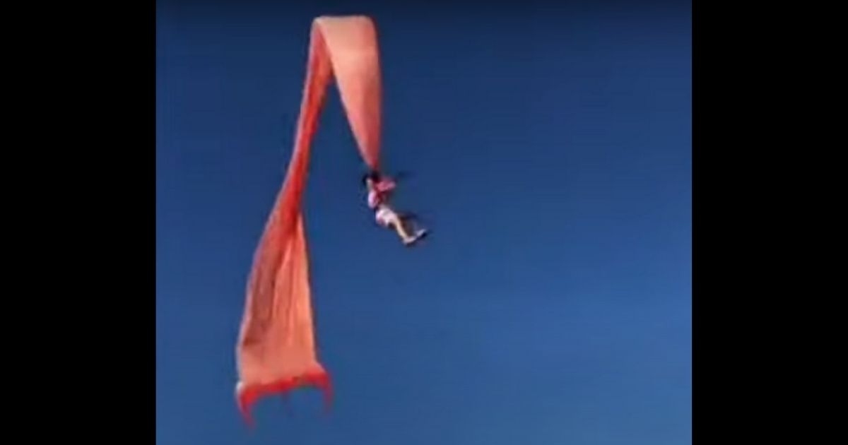Girl attached to kite flying through air