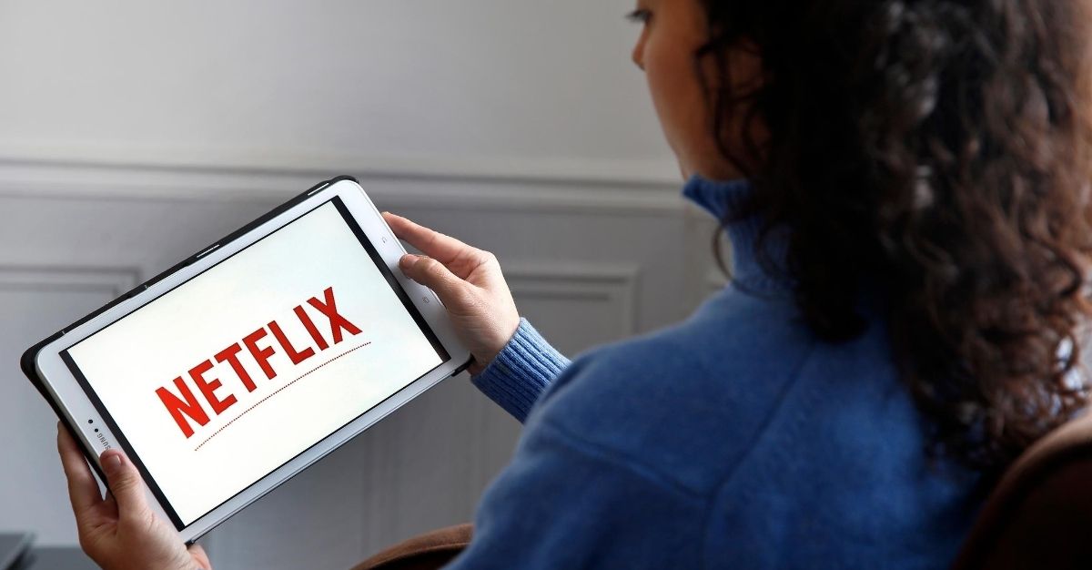 A girl holding a tablet, watching Netflix.