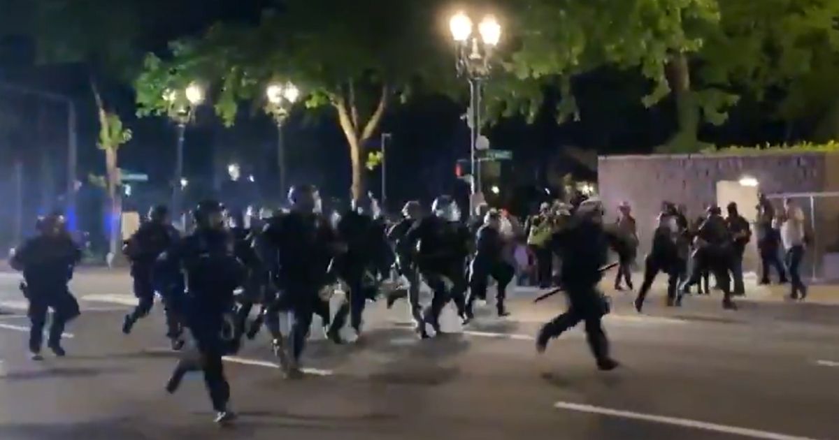 Police in Portland, Oregon, charge a mob gathered in the street with shields.
