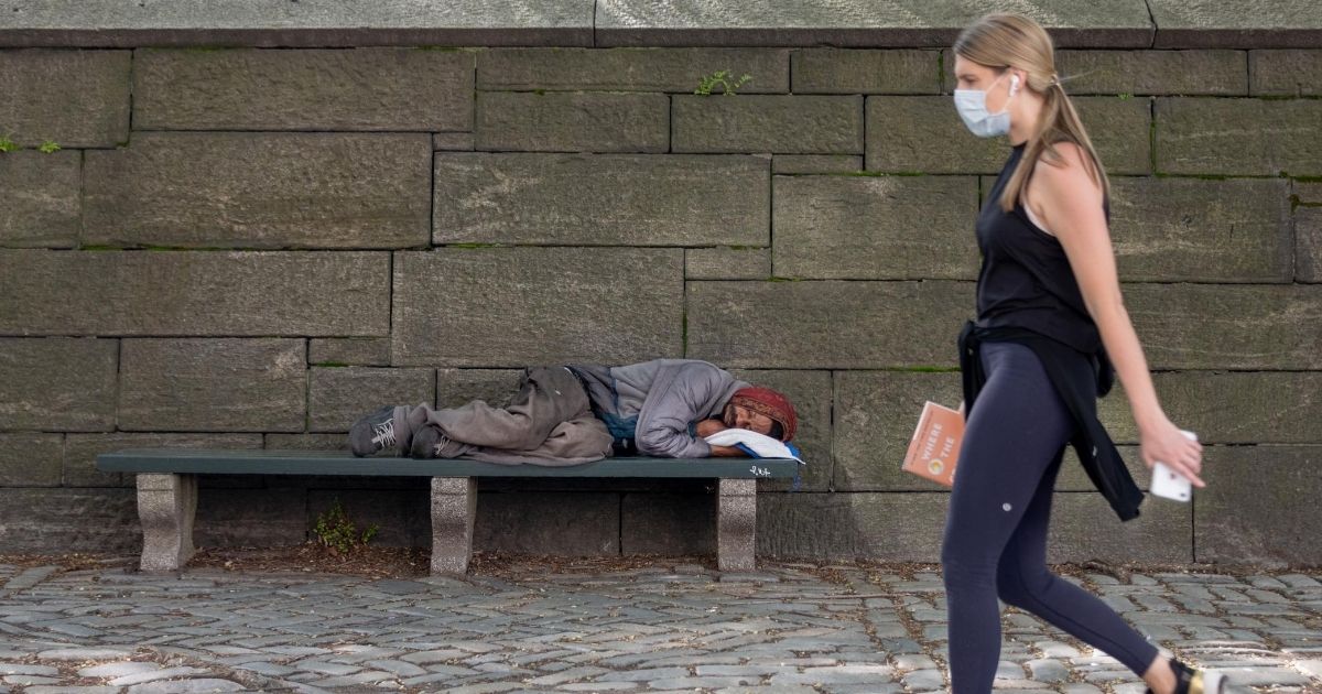 A woman wearing a mask walks past a homeless man sleeping on a bench in New York City in a May 3 file photo.