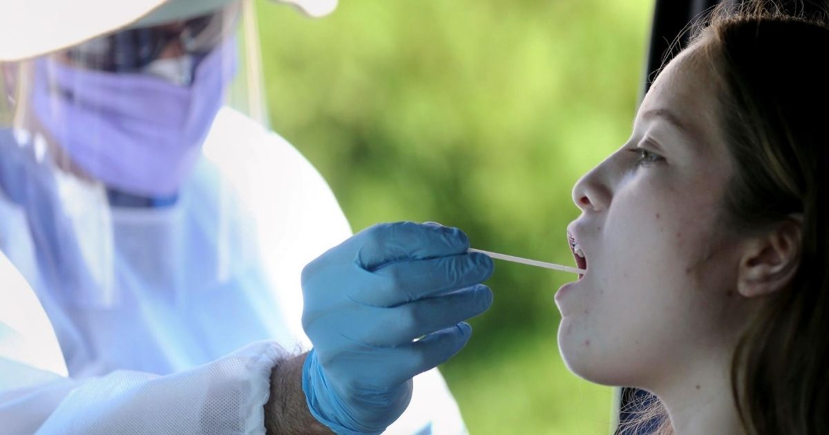 A health care worker gives a girl a throat swab test at a drive-in coronavirus testing center at M.T.O. Shahmaghsoudi School of Islamic Sufism on Aug. 11, 2020, in Los Angeles.