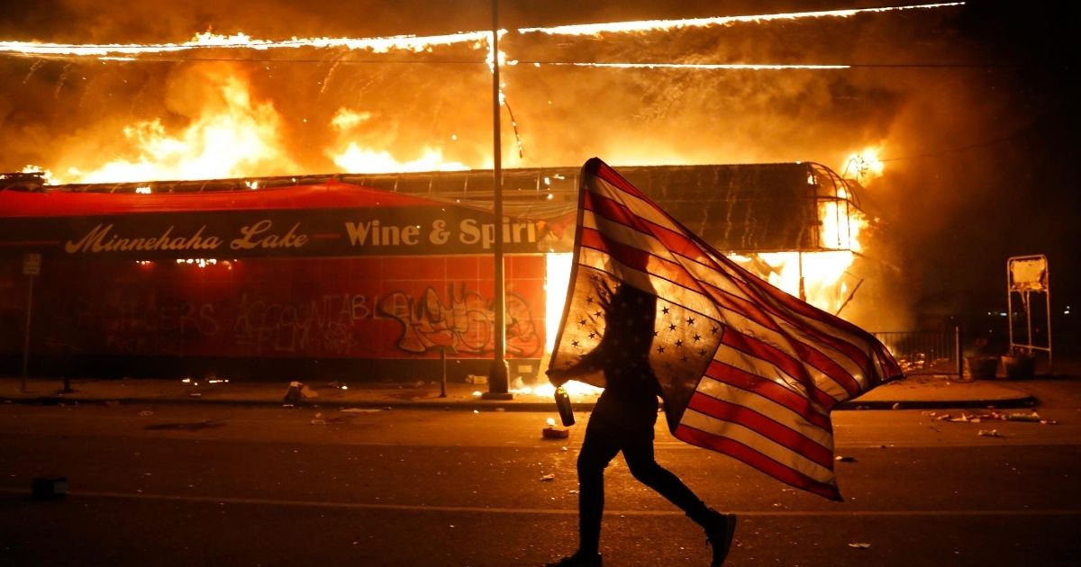A protester carries a U.S. flag upside down, a sign of distress, next to a burning building during a May 28 riot in Minneapolis over the death of George Floyd.