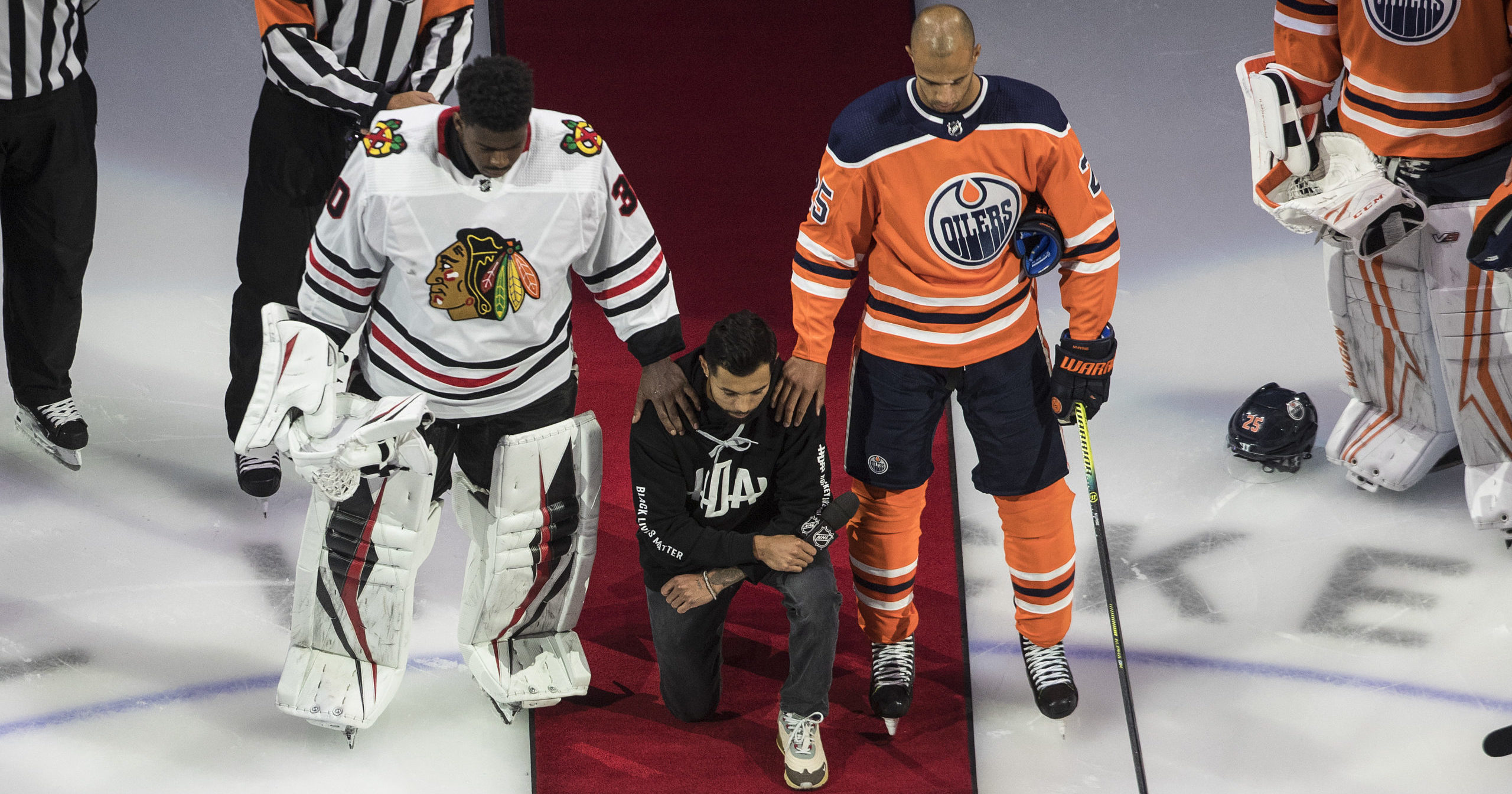 The Minnesota Wild's Matt Dumba takes a knee during the national anthem flanked by the Edmonton Oilers' Darnell Nurse, right, and the Chicago Blackhawks' Malcolm Subban before an NHL hockey game in Edmonton, Alberta on Aug. 1, 2020.