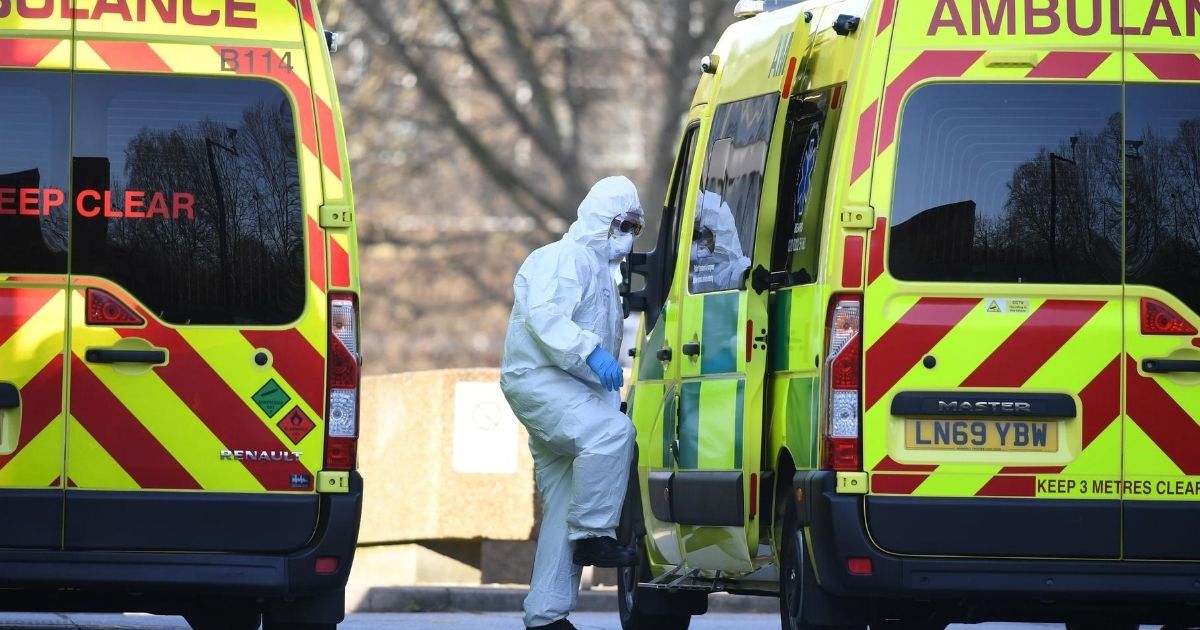 A member of the ambulance service wearing personal protective equipment is seen leading a patient into an ambulance at St Thomas' Hospital in London on March 24, 2020.