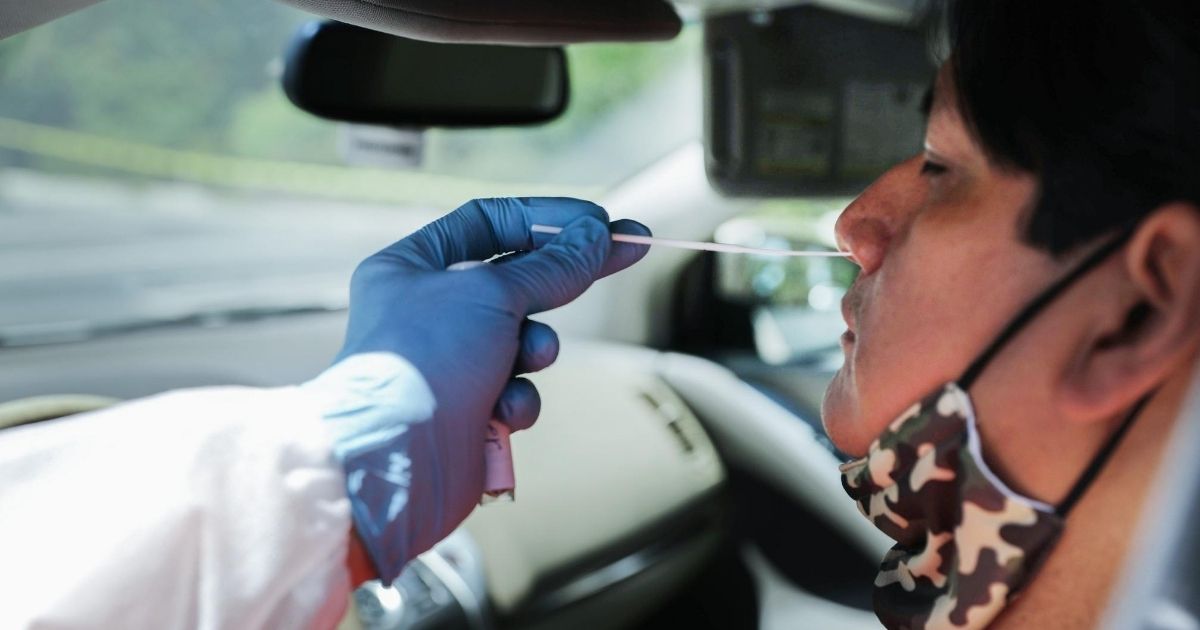 A health care worker gives a motorist a nasal swab test at a drive-in coronavirus testing center at M.T.O. Shahmaghsoudi School of Islamic Sufism on Aug. 11, 2020, in Los Angeles, California.