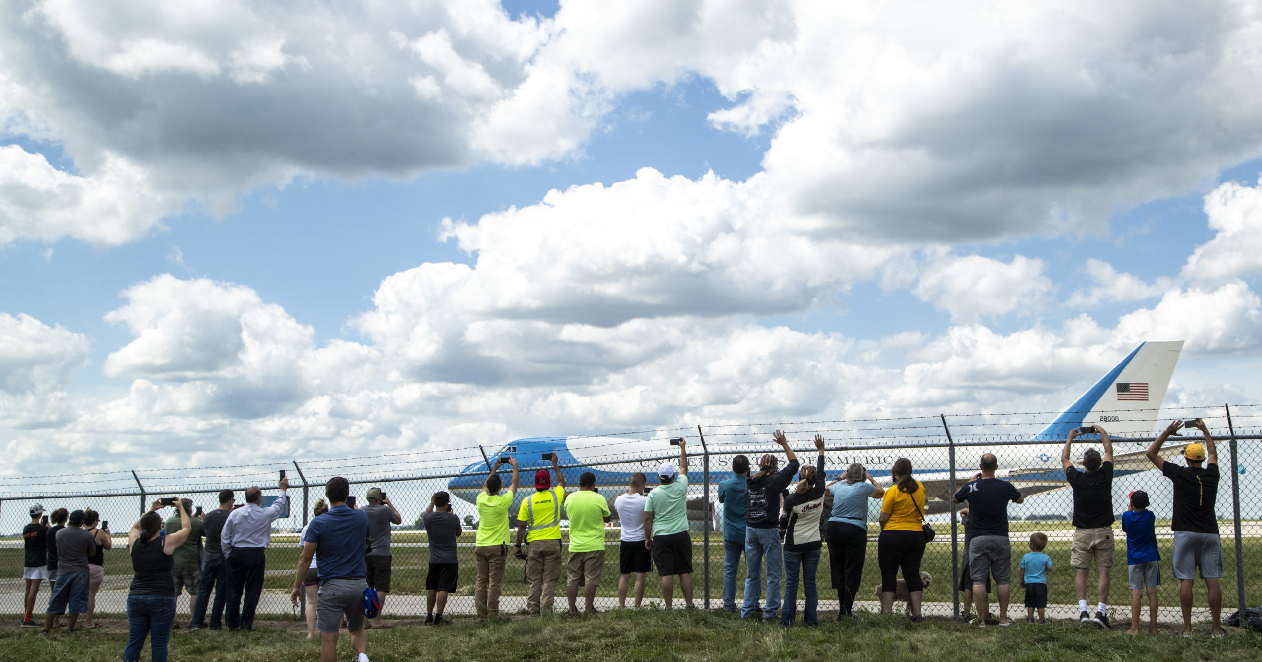 People lean up against a fence as Air Force One takes off on Aug. 18, 2020, after President Donald Trump visited with Iowa leaders in Cedar Rapids, Iowa. Trump attended a disaster recovery briefing at the airport in Cedar Rapids, one of the cities hit hardest by the Aug. 10 derecho that caused extensive damage to electricity infrastructure, homes and farms.