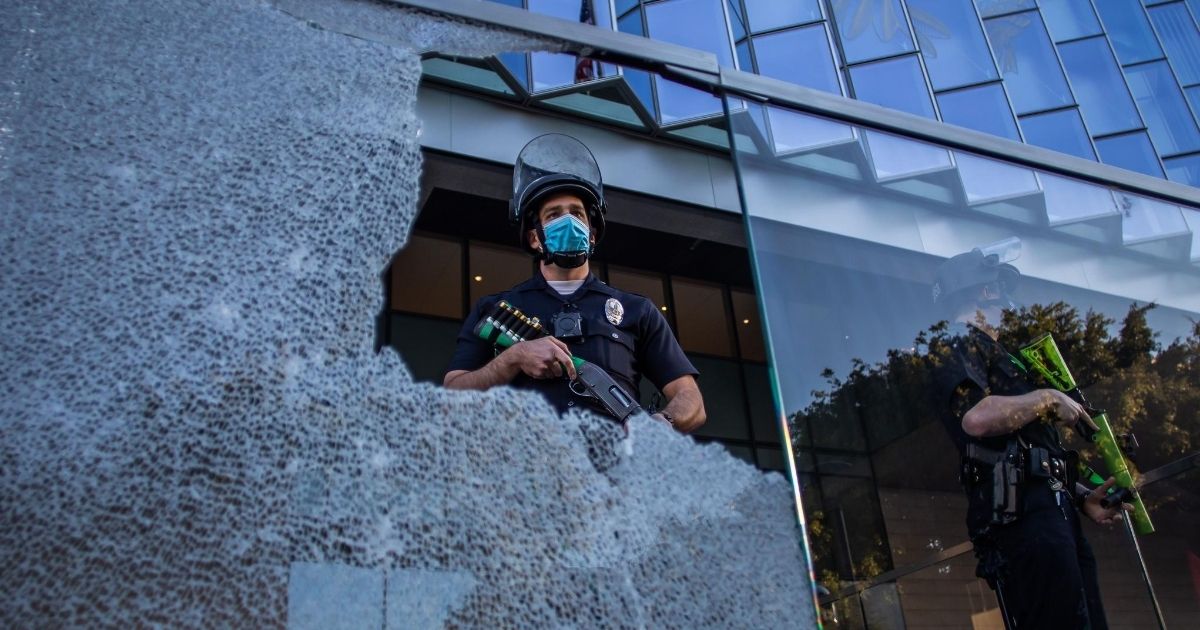 A police officer is seen through broken glass during a protest in downtown Los Angeles, California, on July 25, 2020.
