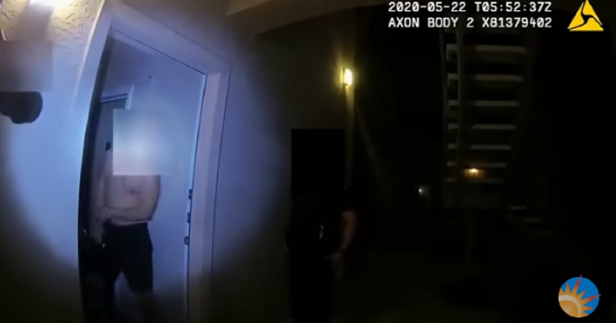 A man answers an apartment door bathed in a police officer's flashlight glare.