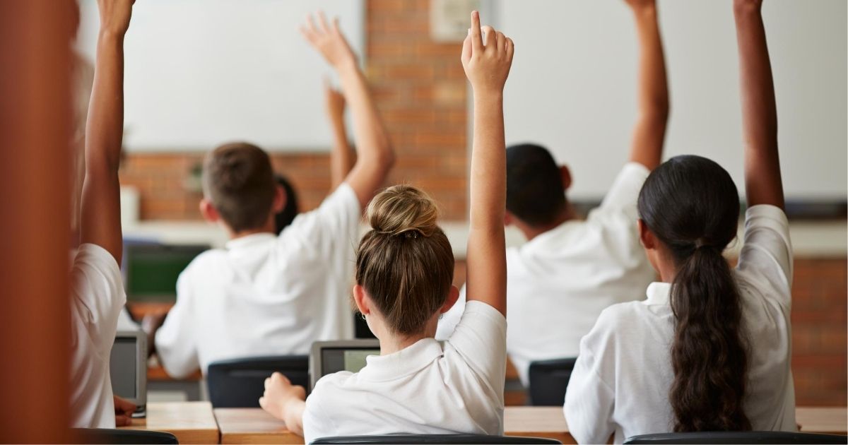 School children raise their hands in this stock photo.