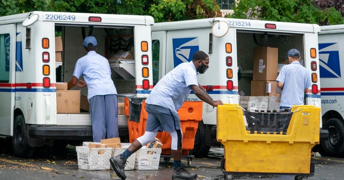 In this July 31, 2020, file photo, letter carriers load mail trucks for deliveries at a US Postal Service facility in McLean, Virginia.