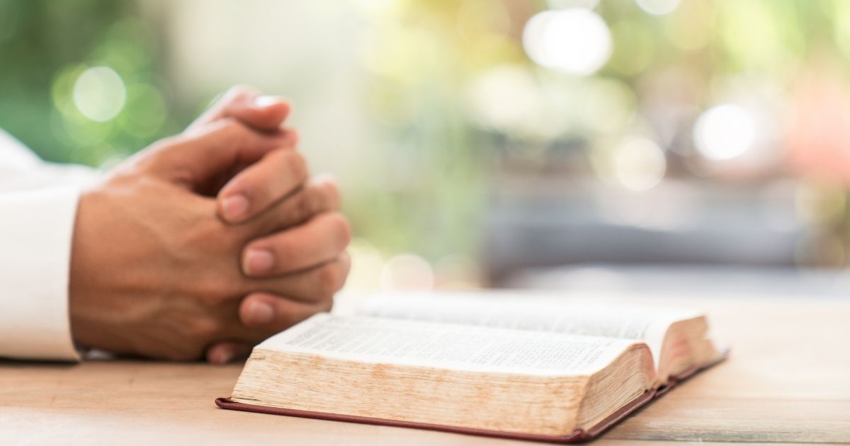 A man prays next to a Bible in the stock image above.