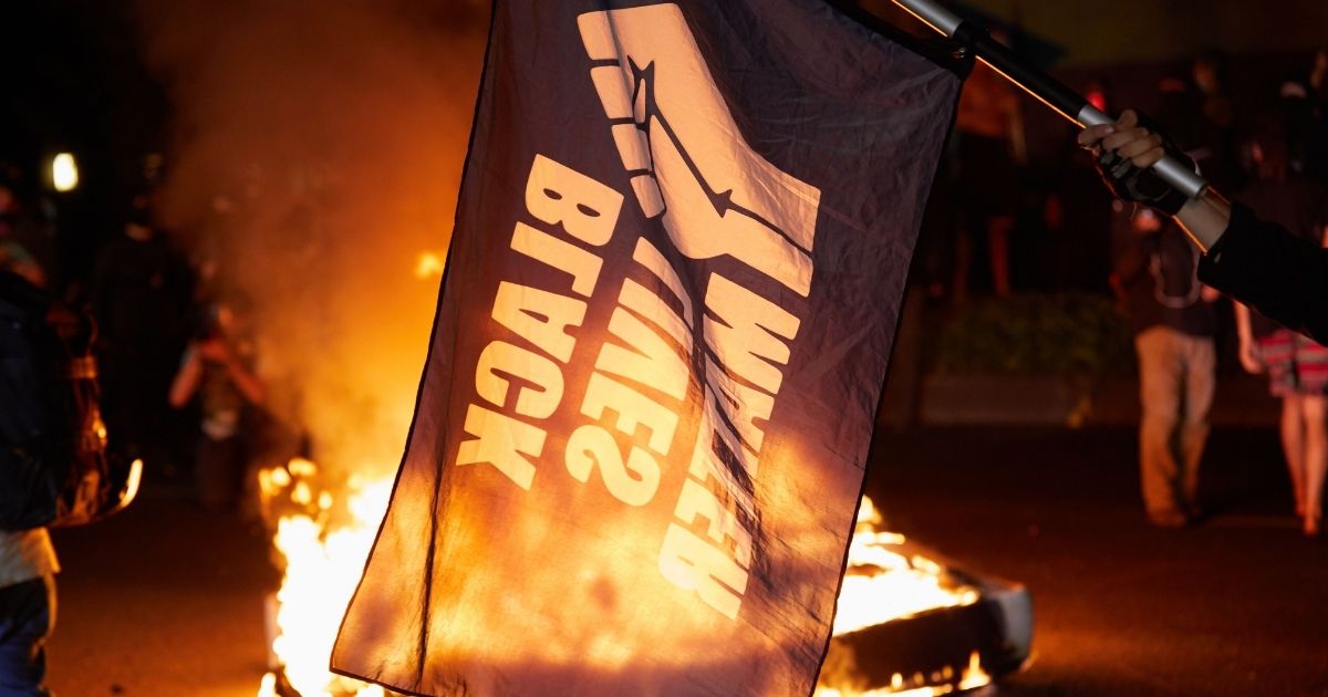 A Black Lives Matter flag waves in front of a fire at the North Precinct Police building in Portland, Oregon, on Sept. 6, 2020.