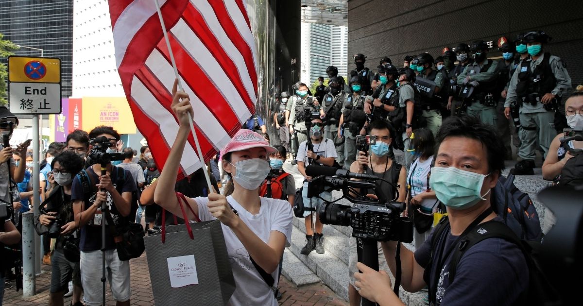 A woman carries an American flag during a protest outside the U.S. Consulate in Hong Kong. The U.S. has issued a new advisory Tuesday, Sept. 15, 2020, warning against travel to mainland China and Hong Kong, citing the risk of "arbitrary detention" and 'arbitrary enforcement of local laws.'