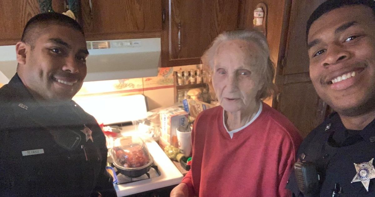 Two officers pose with a 92-year-old who lives alone and had little food in her house. They bought her groceries and started a fundraiser to help improve her stability and comfort.