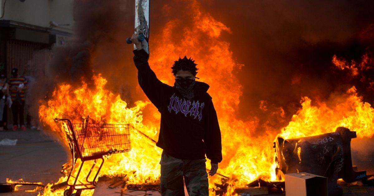 A man holds a skateboard in front of a fire in Los Angeles on May 30, 2020.