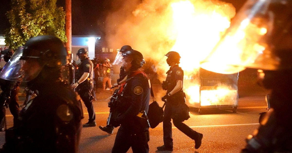 Portland police walk past a dumpster fire during a crowd dispersal on Aug. 14, 2020, in Portland, Oregon.