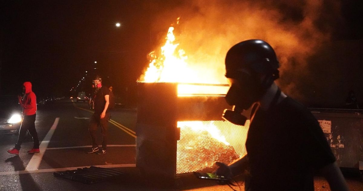 Demonstrators walk past a dumpster fire during another night of rioting in Portland, Oregon, on Aug. 14, 2020.