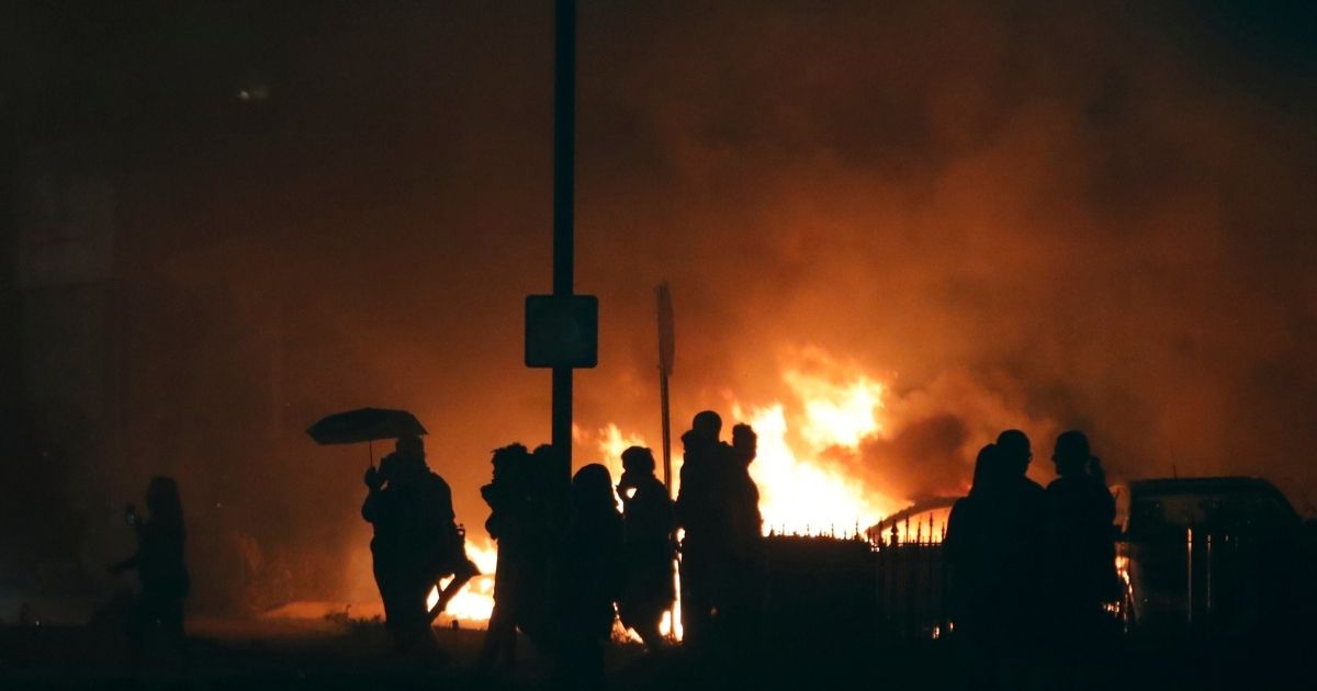 The silhouettes of the demonstrators outline against the glowing flames of cars they set on fire a few blocks from the County Court House during a demonstration against the shooting of Jacob Blake, who was shot in the back multiple times by police the day before, prompting community protests in Kenosha, Wisconsin, on Aug. 24, 2020.