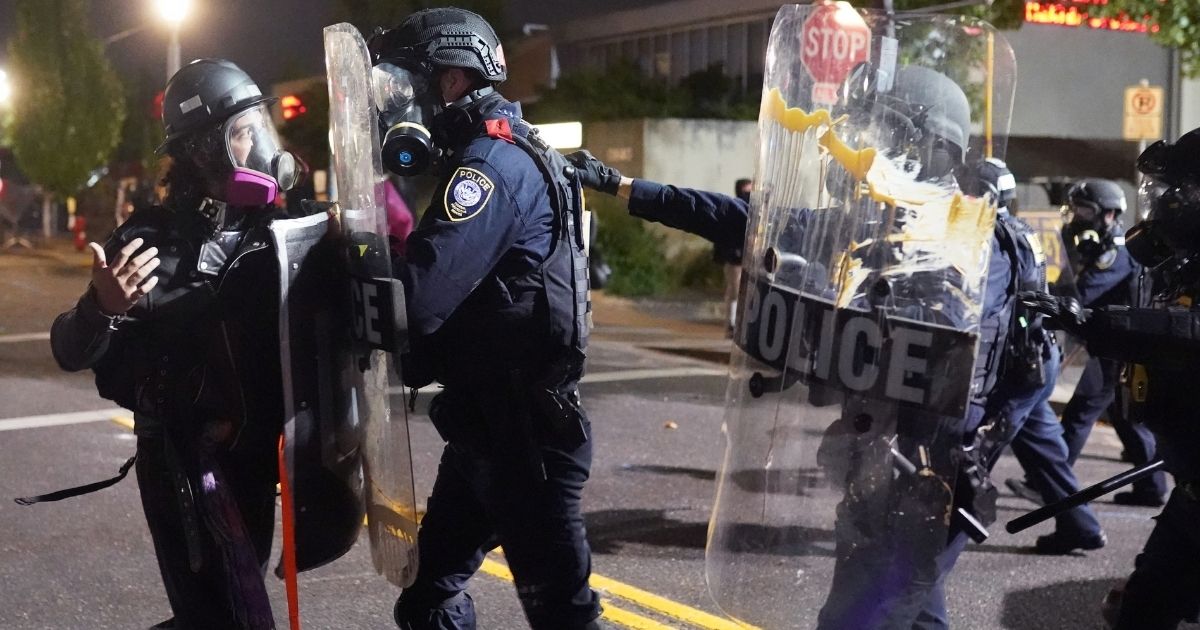 PORTLAND, OR - AUGUST 20: Federal officers use riot shields to push a protester while dispersing a crowd of about 150 people from in front of the Immigration and Customs Enforcement (ICE) detention facility on August 20, 2020 in Portland, Oregon. For the second night in a row federal police clashed with crowds in South Waterfront after being absent from Portlands nightly protest for weeks.