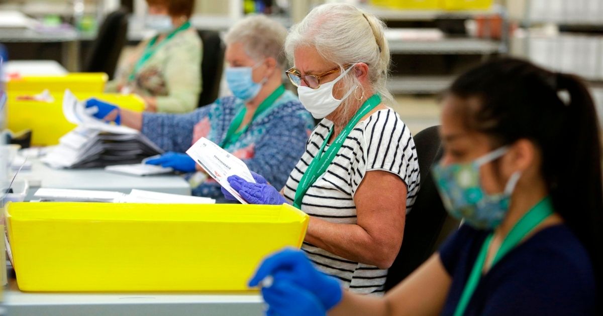 Election workers wear masks and gloves as they open envelopes containing vote-by-mail ballots for the August 4 Washington state primary at King County Elections in Renton, Washington on August 3, 2020.