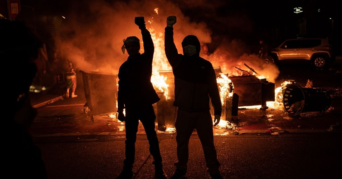 SEATTLE, WA - JUNE 08: Demonstrators raise their fists as a fire burns in the street after clashes with law enforcement near the Seattle Police Departments East Precinct shortly after midnight on June 8, 2020 in Seattle, Washington. Earlier in the evening, a suspect drove into the crowd of protesters and shot one person, which happened after a day of peaceful protests across the city. Later, police and protesters clashed violently during ongoing Black Lives Matter demonstrations following the death of George Floyd.